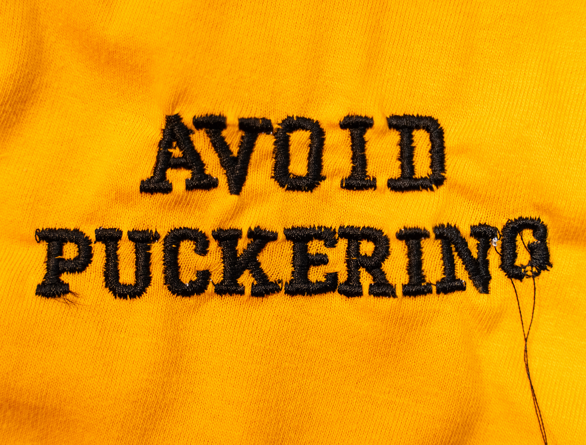 avoidingpuckering | Embroidery Legacy the words "Avoid Puckering" stitched out on orange fabric showcasing puckering issues