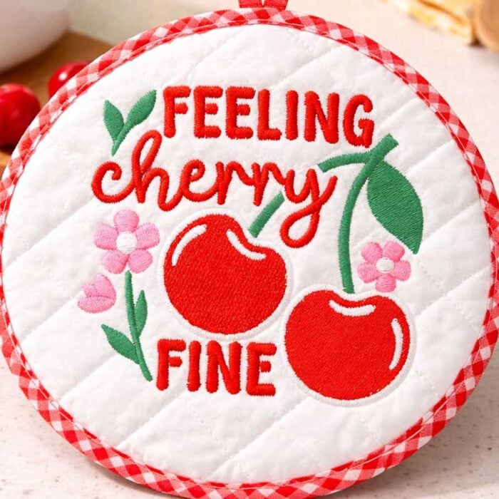 SD_SF_04_HotPad | Embroidery Legacy Round quilted white coaster with red cherries, flowers, and the embroidered text 'FEELING cherry FINE' along a red gingham edge.