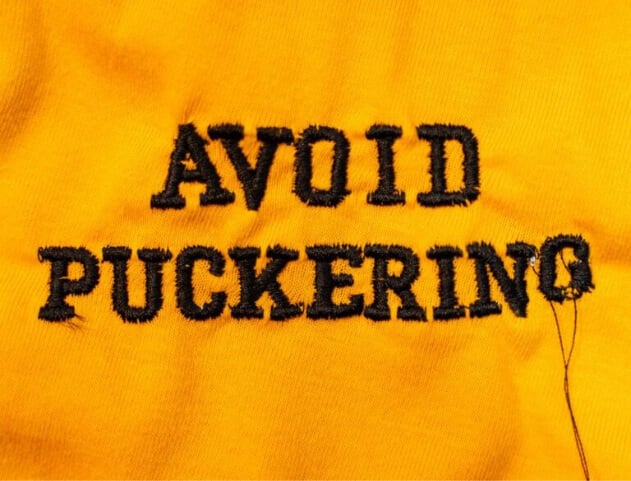 embroidery-digitizing-avoid-puckering-mobile | Embroidery Legacy the words "Avoid Puckering" stitched out on orange fabric showcasing puckering issues