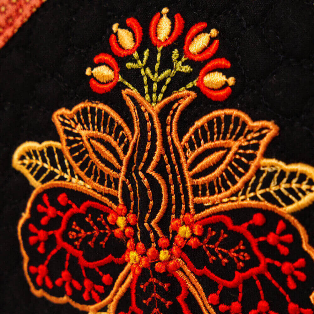 Artboard49 1 1 1 Embroidered floral pattern in red and gold on black fabric, bordered by a red patterned edge.