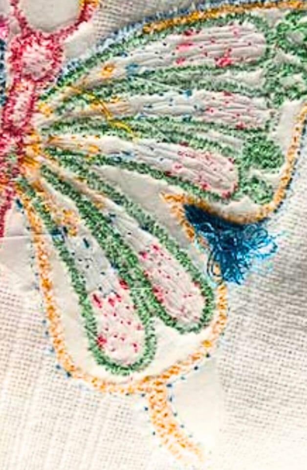Birds-nesting-embroidery-design-mobile | Embroidery Legacy Close-up of a multicolored butterfly embroidery on white fabric, with green, pink, orange and blue thread detailing the wings.