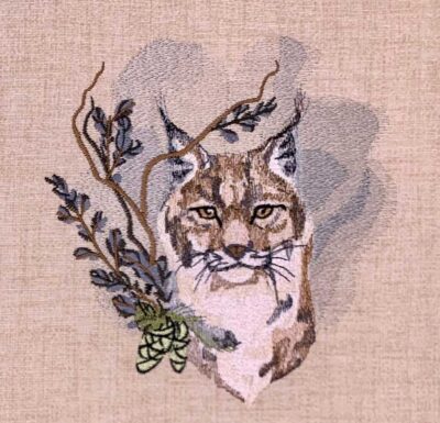 Embroidered image of a lynx head with branches and leaves on a beige fabric background, in brown and tan tones.