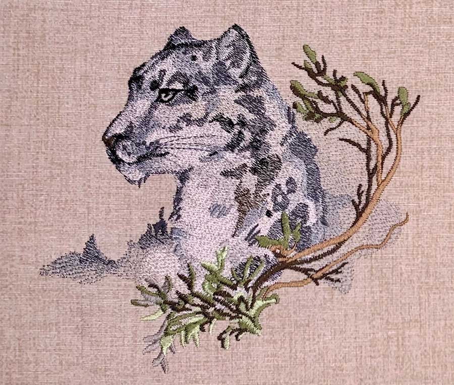 Embroidered wolf head in profile on a branch with green leaves on beige fabric