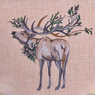 Embroidered illustration of a reindeer with large branching antlers on beige fabric with greenery around its neck