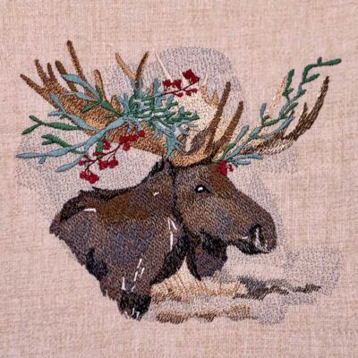 Embroidered tapestry showing two moose heads with antlers adorned with greenery and red berries on a beige background.
