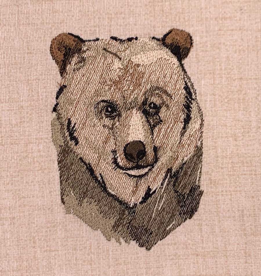 Embroidery of a bear's head on beige fabric, close-up view.