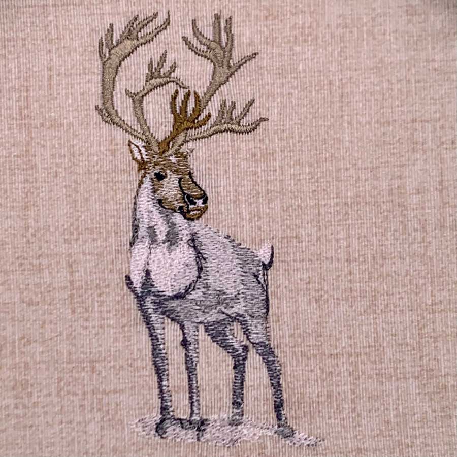 Embroidered illustration of a standing reindeer with large antlers on beige fabric
