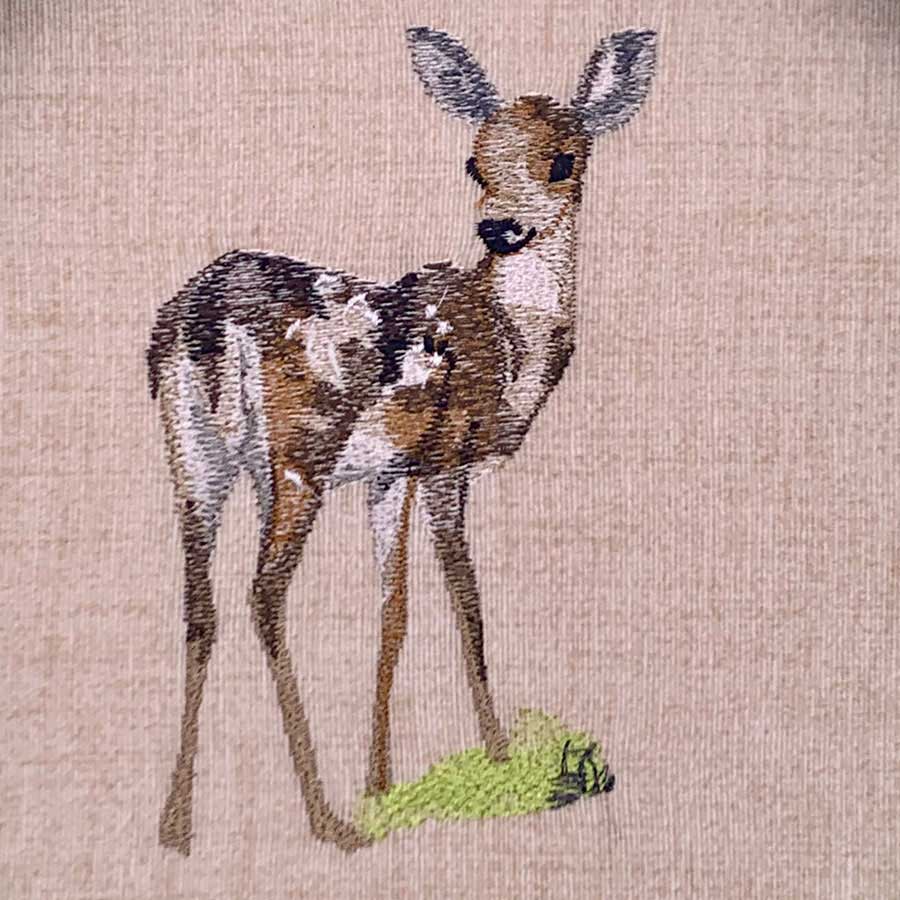 Embroidery of a kangaroo standing on a small patch of grass on beige fabric, in brown and gray tones
