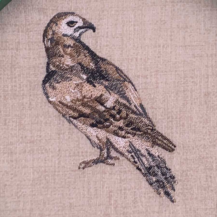 Brown and white embroidered bird perched on beige fabric background, decorative textile detail.