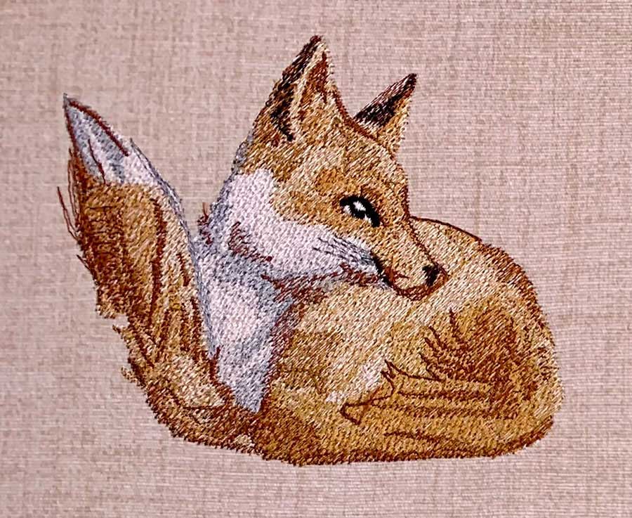Embroidered tapestry showing a curled fox with tan and white fur on a pink-beige background, facing left.