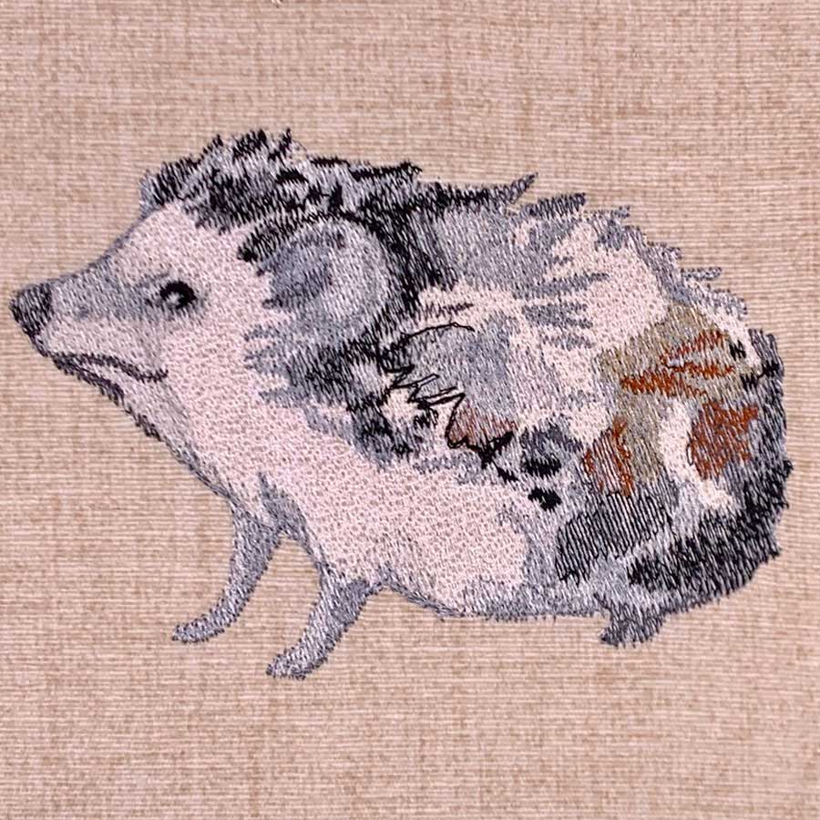 Embroidery of a pig facing left on a beige fabric background with gray, black, and brown patchwork patterns.