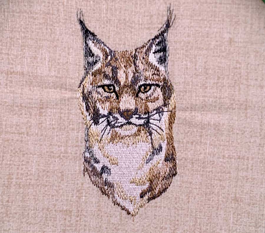 Embroidery artwork of a bobcat's head on a light tan fabric.