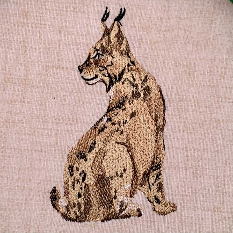 Embroidery of a seated lynx-like wildcat with tufted ears on beige fabric