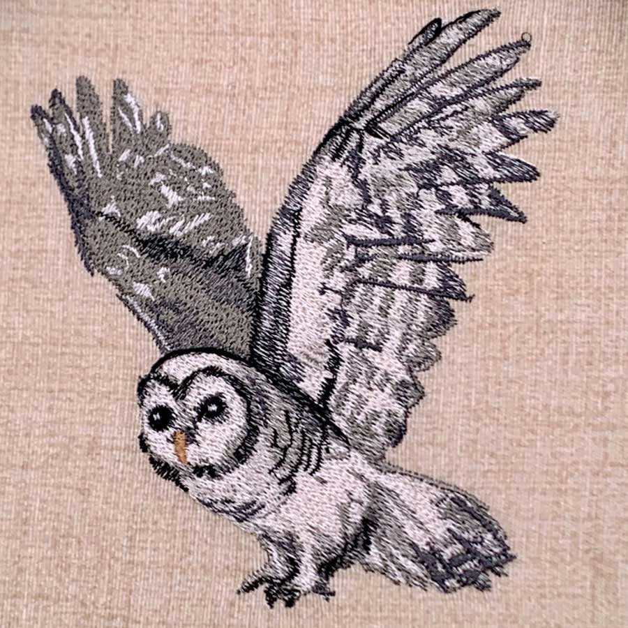 Embroidered owl in flight with outstretched wings on beige fabric