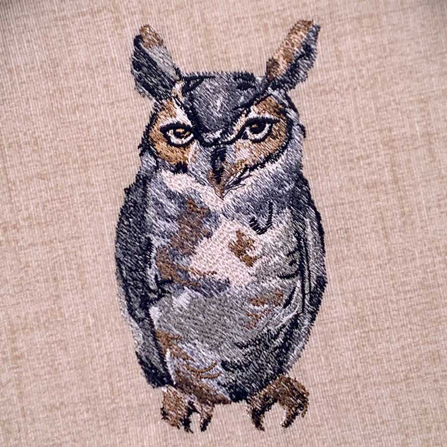 Embroidered owl on beige fabric with gray-brown feathers and yellow eyes (decorative design).