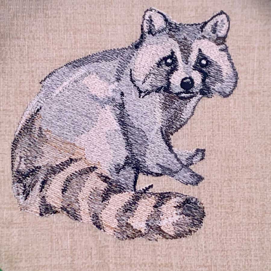 Cartoon raccoon sitting with striped tail, embroidered on beige fabric