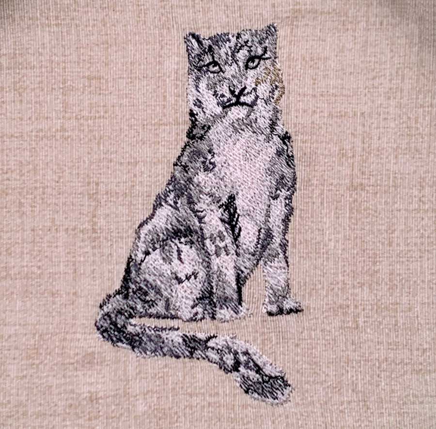 Embroidered illustration of a cat sitting on beige fabric, created with black and gray thread.