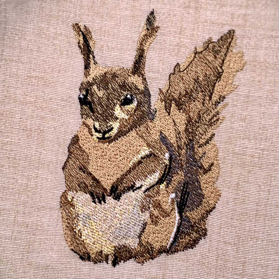 Embroidery of a brown rabbit with ears upright, facing forward, on beige fabric.
