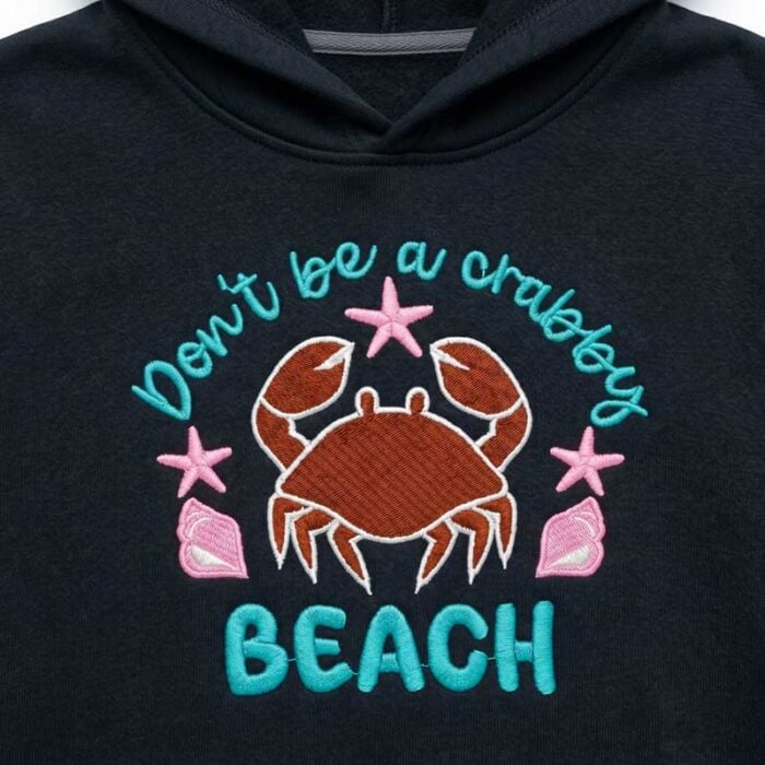 SDSB_DontBeCrabby_Sweatshirt | Embroidery Legacy Navy hoodie featuring teal text reading 'don't be a crabby' circling a brown embroidered crab with pink seashells and starfish, and a teal 'BEACH' at the bottom.