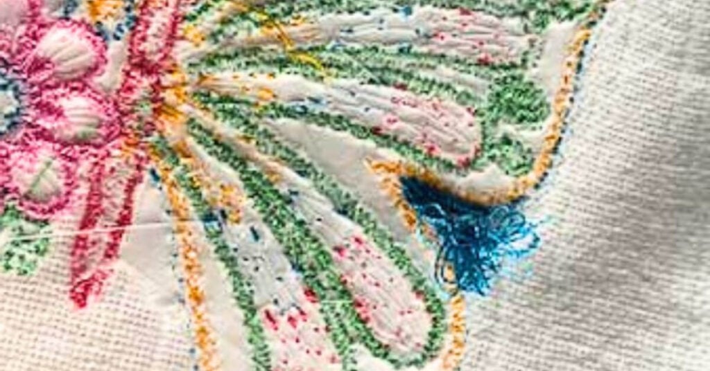 birds-nesting-embroider-design | Embroidery Legacy Close-up of vibrant embroidery on fabric with pink, green, yellow threads and a blue tassel.