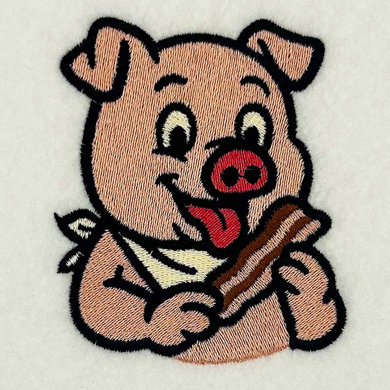 EL_CA_Pig | Embroidery Legacy Cute embroidered pig patch holding a bone with its tongue out on light fabric valuewise playful image