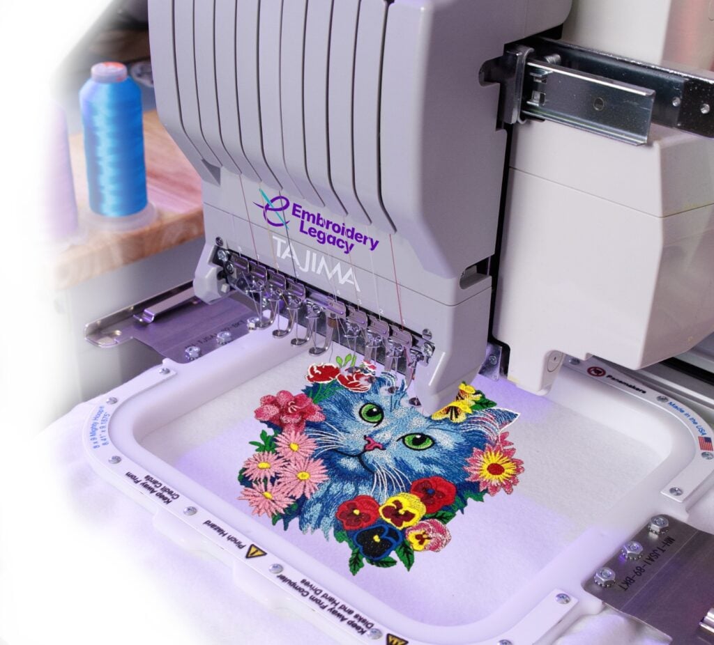 Homepage-cover image-Desktop-v4 Industrial embroidery machine stitching a colorful cat and flower design in a hoop.