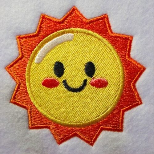 freebie-sun-square | Embroidery Legacy Smiling embroidered sun patch with a yellow face, orange rays, and rosy cheeks on light fabric.