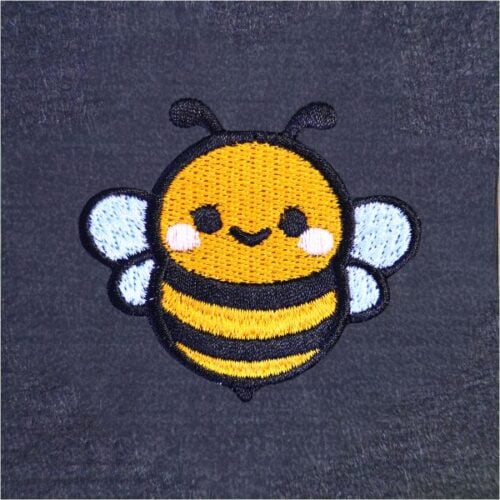 freebie-bee-square | Embroidery Legacy Cute embroidered bee patch with a yellow body, black stripes, white wings, and pink cheeks on a dark fabric background.