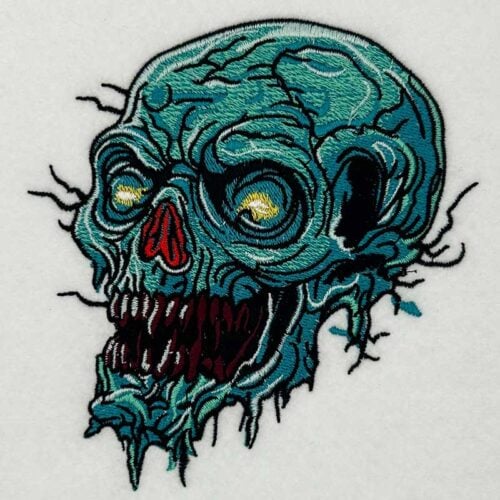 EL_CreepySkull4 | Embroidery Legacy Teal zombie skull embroidery patch with yellow eyes and jagged teeth on white fabric.
