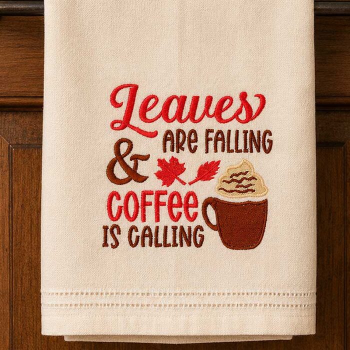 SDFB_LeavesFalling_Towel | Embroidery Legacy Embroidered kitchen towel with autumn message: "Leaves are falling & coffee is calling" and a coffee cup illustration on a beige towel.