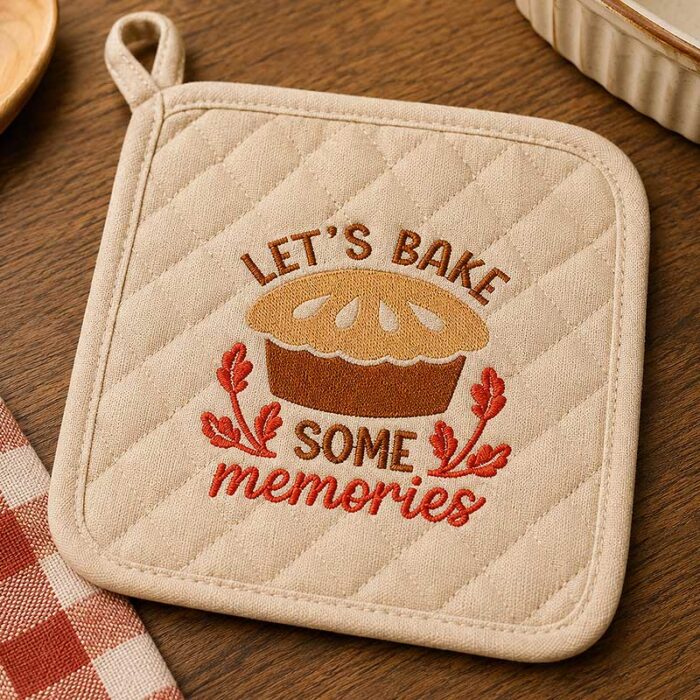 SDFB_LetsBakeMemories_HotPad | Embroidery Legacy Quilted beige potholder with an embroidered loaf of bread and the words 'Let's bake some memories' on a wooden table.