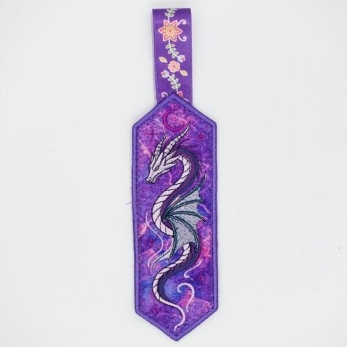 freebie-design-dragon-bookmark-ith | Embroidery Legacy Purple bookmark with a silver dragon illustration and a floral ribbon hanger at the top.