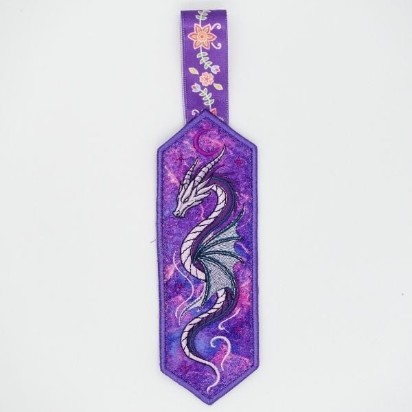 freebie-design-dragon-bookmark-ith | Embroidery Legacy Purple bookmark with a silver dragon illustration and a floral ribbon hanger at the top.